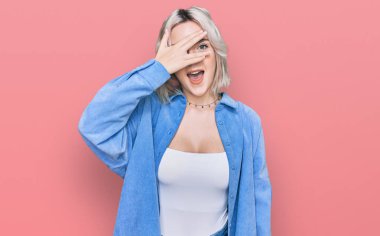 Sıradan kıyafetler giyen genç sarışın kız şok içinde yüzünü ve gözlerini kapayarak utanmış bir ifadeyle parmaklarının arasından bakıyor.. 