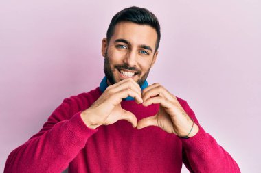 Gündelik kıyafetler giyen, aşık gülümseyen, elleriyle kalp sembolü yapan genç bir İspanyol. romantik kavram. 