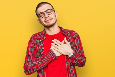Latin asıllı genç adam gündelik kıyafetler giyiyor elleri göğsünde, gözleri kapalı gülümsüyor ve yüzünde minnet ifadesi var. sağlık kavramı. 