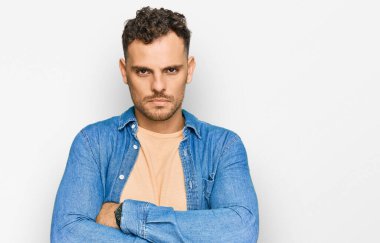 Gündelik kıyafetler giyen, kuşkucu ve gergin genç İspanyol bir adam. Yüzünde çapraz kollarla onaylamayan bir ifade var. negatif kişi. 