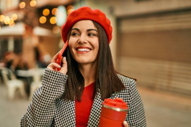 Genç İspanyol kadın akıllı telefondan konuşuyor ve şehirde kahve içiyor..