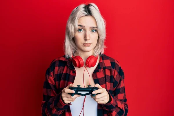 年轻的金发姑娘玩电子游戏时 抱着控制者的怀疑和紧张 皱着眉头因问题而心烦意乱 消极的人 — 图库照片