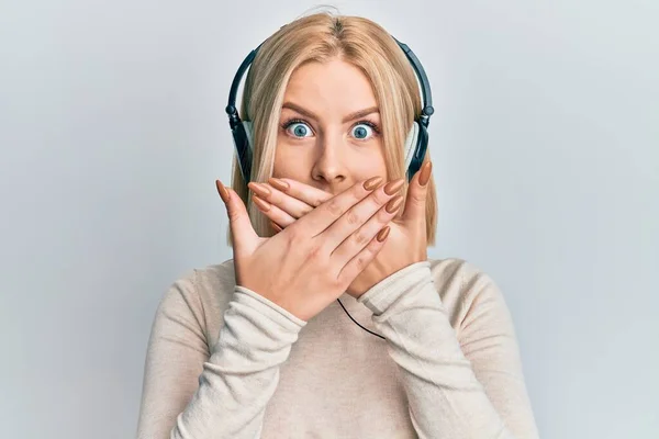 Mujer Rubia Joven Escuchando Música Usando Auriculares Impactados Cubriendo Boca —  Fotos de Stock
