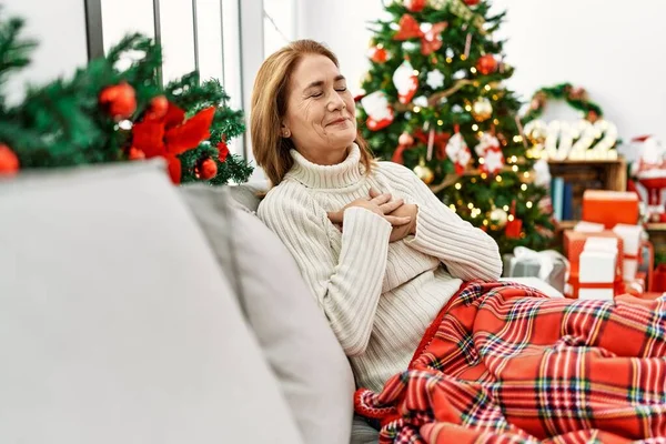中世の女性は目を閉じて胸に手で笑みを浮かべてクリスマスツリーでソファの上に座って 顔に感謝のジェスチャー 健康の概念 — ストック写真