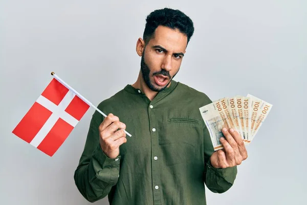 Młody Hiszpan Trzymający Flagę Denmarkową Banknoty Koronowe Szokującej Twarzy Wyglądający — Zdjęcie stockowe