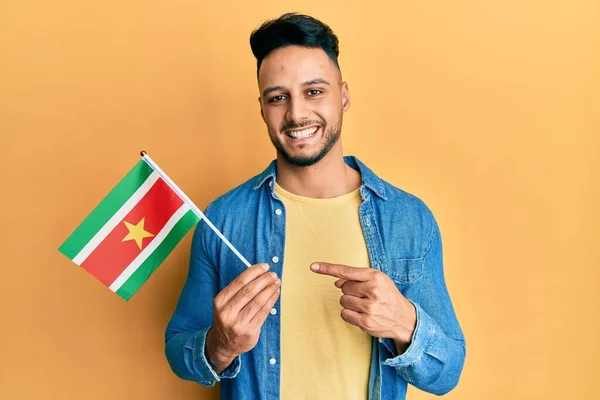 Joven Árabe Sosteniendo Bandera Surinam Sonriendo Feliz Señalando Con Mano —  Fotos de Stock