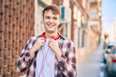 Genç beyaz adam şehirde kulaklık takarak mutlu bir şekilde gülümsüyor..