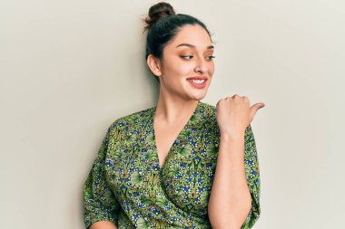 Güzel bir orta doğulu kadın, günlük kıyafetler giyip baş parmağını yana kaldırıyor ve ağzı açık gülümsüyor. 