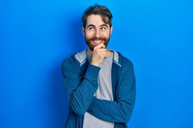 Sakallı, sıradan bir kazak giyen, eli çenesinde soru soran, düşünceli bir beyaz adam. Düşünceli bir yüzle gülümsüyor. şüphe kavramı. 