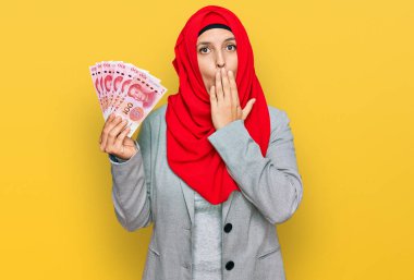 İslami tesettüre bürünmüş güzel İspanyol bir kadın Çin Yuan banknotları tutuyor. Ağzını eliyle kapatıyor, şok geçiriyor ve hata yapmaktan korkuyor. şaşırmış ifade 