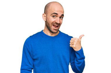 Gündelik kıyafetler giyen, gülümseyen, gülümseyen ve başparmağıyla yan tarafı gösteren İspanyol genç adam.. 