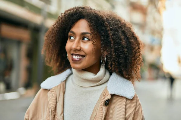 Genç Afrikalı Amerikalı kadın gülümseyerek şehirde mutlu mesut duruyor..