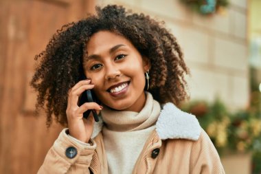 Genç Afrikalı Amerikalı kadın gülümsüyor. Şehirdeki akıllı telefondan mutlu bir şekilde konuşuyor..