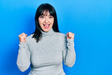 Gündelik giysiler giyen genç İspanyol kadın şaşkınlık ve şaşkınlık içinde kollarını kaldırarak ve gözlerini açarak başarıyı kutluyor. Kazanan konsept. 