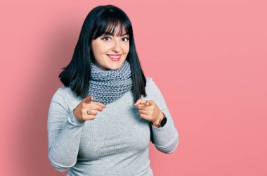 Genç İspanyol artı kışın atkı takan kadın mutlu ve komik yüzlü parmaklarını kameraya doğrultuyor. iyi enerji ve titreşimler. 