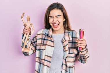 Küçük tahta manikin ve kalemler tutan genç beyaz kız kahkahalarla gülüyor.. 