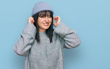 Gürültülü müzik sesi için sevimli yün şapkalı, parmaklarıyla kulaklarını kapatan rahatsız edici ifadeli genç İspanyol kadın. sağır kavramı. 