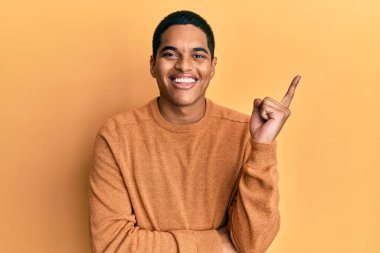 Genç, yakışıklı, sıradan bir süveter giyen, yüzünde kocaman bir gülümseme olan, elleri ve parmaklarıyla kameraya bakan İspanyol bir adam.. 