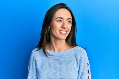 Günlük kıyafetler giyen genç İspanyol kız yüzünde gülümsemeyle yan yana bakıyor, doğal bir ifade. Kendinden emin gülen. 