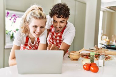 Mutfakta dizüstü bilgisayar kullanarak mutlu gülümseyen genç çift..