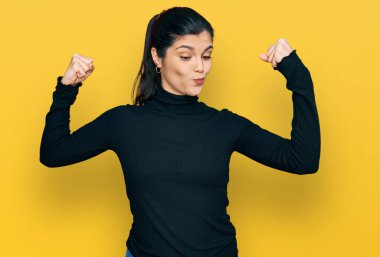 Sıradan kıyafetler giyen genç İspanyol kadın gururla gülümseyen kol kaslarını gösteriyor. fitness konsepti. 