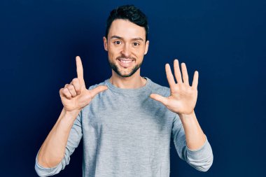 Gündelik kıyafetler giyen genç İspanyol adam yedi numarayı gösterip işaret ederken kendinden emin ve mutlu bir şekilde gülümsüyor.. 