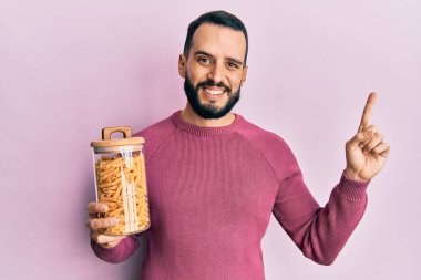 Sakallı genç adam elinde makarna kavanozuyla gülümsüyor. 