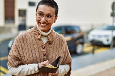 Kısa saçlı güzel İspanyol bir kadın mutlu bir şekilde gülümsüyor. Elinde Norveç banknotları olan bir cüzdan tutuyor.