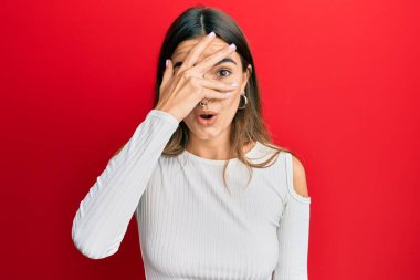 Gündelik kıyafetler giyen genç İspanyol kadın şok içinde yüzünü ve gözlerini eliyle kapatıyor, parmaklarından korkuyla bakıyor. 