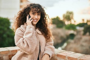 Genç İspanyol kadın gülümsüyor. Şehirdeki akıllı telefondan konuşuyor.