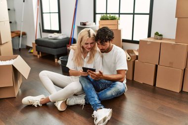 Genç ve güzel bir çift yeni evinde dokunmatik ped kullanarak mutlu bir şekilde gülümsüyor..