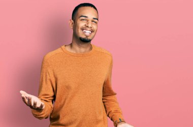 Genç Afrikalı Amerikalı günlük kıyafetler giymiş neşeli kollarını açıp gülümseyen bir adam. Hoş geldin, olumlu ve kendinden emin selamlar. 