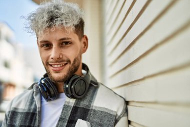 Şehirde kulaklık takarak mutlu gülümseyen genç İspanyol adam..