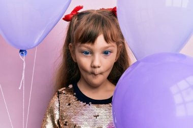 Küçük beyaz kız balon tutuyor. Ağızlarıyla balık yüzü yapıyor. Gözlerini kıstı.. 