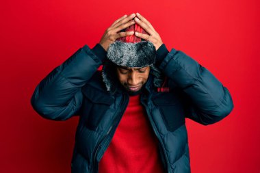 Sakallı, kışlık şapkalı ve paltolu genç Afrikalı Amerikalı adam acı ve migren yüzünden çaresiz ve stresli bir baş ağrısı çekiyor. Eller başının üstünde.. 