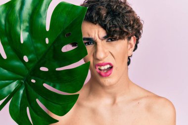 Yeşil yaprak tutan genç bir adam makyaj şok yüzünde güzel bir yüz, şüpheci ve alaycı görünüyor, açık ağızla şaşırmış 