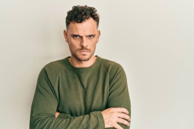 Gündelik kıyafetler giyen, kuşkucu ve gergin genç İspanyol bir adam. Yüzünde çapraz kollarla onaylamayan bir ifade var. negatif kişi. 