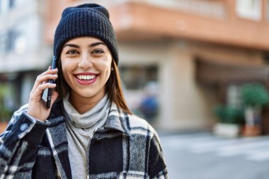 Genç İspanyol kadın gülümsüyor. Şehirdeki akıllı telefondan konuşuyor..