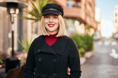 Genç sarışın kadın gülümsüyor, mutlu bir şekilde şehirde duruyor..