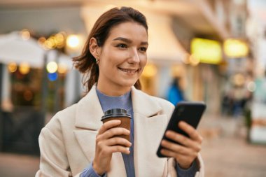 Genç İspanyol kadın akıllı telefon kullanıyor ve şehirde kahve içiyor..