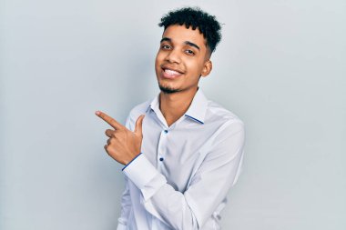 Genç Afro-Amerikan adam iş gömleği giyiyor. Gülümsüyor, gülümsüyor. Elleri ve parmakları yana bakıyor. 