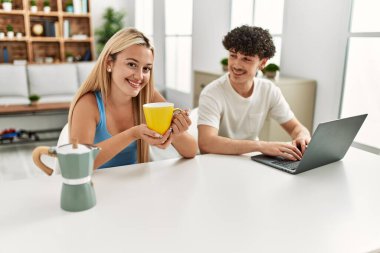 Genç çift dizüstü bilgisayar kullanıyor ve evde kahve içiyor..