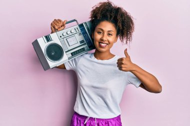 Güzel, afro saçlı, antreman kıyafetleri giyen, elinde teyp teybi tutan mutlu ve pozitif gülümseyen, başparmağını kaldırıp mükemmel bir iş çıkaran afro-amerikalı kadın. 