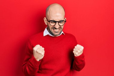 Genç kel adam gündelik kıyafetler ve gözlük takıyor. Çok mutlu ve heyecanlı. Kolları havada, gülümseyen ve başarı için çığlık atan kazanan bir jest yapıyor. kutlama konsepti. 