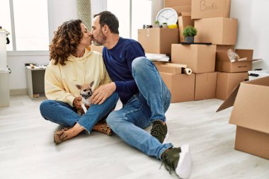 Orta yaşlı, gülümseyen bir İspanyol çift yeni evinde köpekle yerde oturuyor..