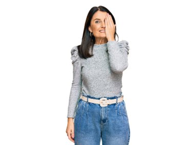 Orta yaşlı esmer kadın gündelik kıyafetler giyiyor. Bir gözünü eliyle kapatıyor. Yüzünde kendine güvenen bir gülümseme ve sürpriz bir duygu var.. 