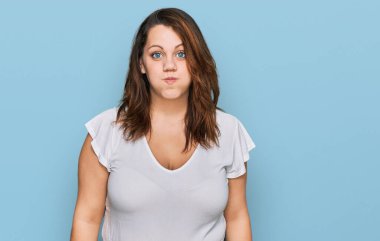 Gündelik beyaz tişört giyen, komik yüzlü, yanak şişiren genç ve uzun boylu bir kadın. Havayla şişmiş ağız, çılgın bir ifade.. 