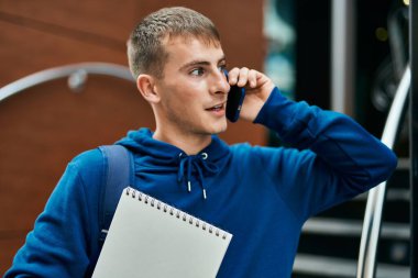 Üniversitede elinde not defteriyle konuşan sarışın genç bir öğrenci..