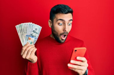 Genç İspanyol adam elinde akıllı telefon, elinde banknotlarla korku ve şaşkınlık dolu bir ifade, korku ve heyecan dolu bir yüz tutuyor.. 