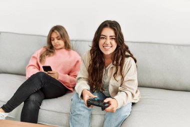 Kız video oyunu oynuyor ve kız arkadaşı evde akıllı telefon kullanıyor..